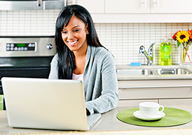 Smiling woman sitting in her kitchen with a cup of coffee working on a laptop
