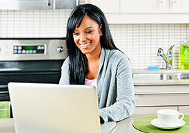 Smiling woman sitting in a kitchen and looking at a laptop