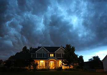 Large suburban home in the evening with lights on and a cloudy sky in the background