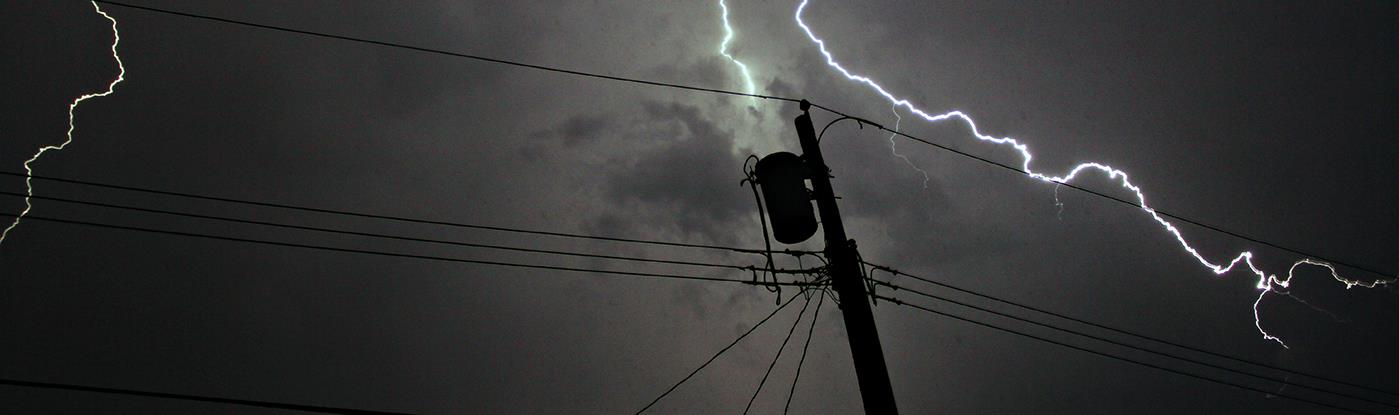 Lightning strike in sky behind a utility pole & wires