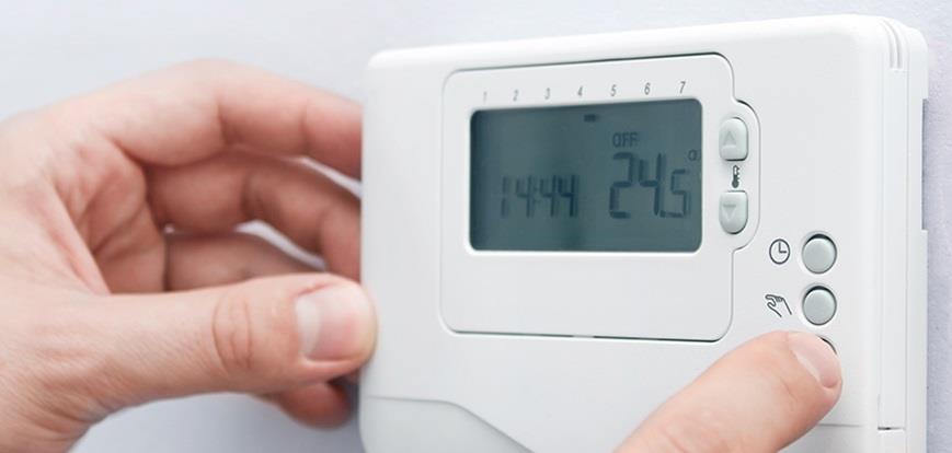Fingers adjusting the settings on a digital thermostat