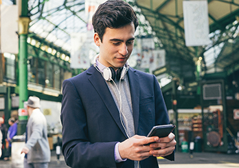 Young, male executive with headphones hanging around his neck, looking at his smartphone