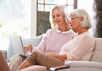 An older and a younger woman sitting together on the couch, looking at a computer