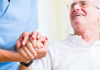 Older man sitting, holding hands with healthcare worker
