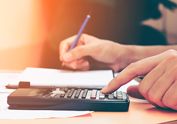 Hands on a table - pen in right hand, left hand touching buttons on a calculator