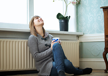 Happy woman sitting on floor leaning against radiator