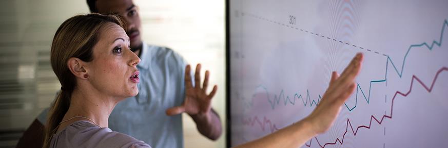 Two people discussing a chart displayed on a smart board.