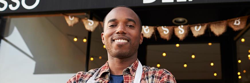 Proud deli owner wearing an apron standing outside his deli