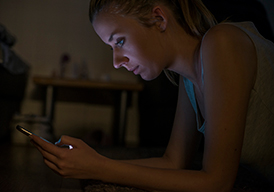 Woman sitting in the dark looking at a smartphone