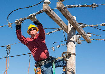 A utility worker connected to the side of a utility pole while repairing wires