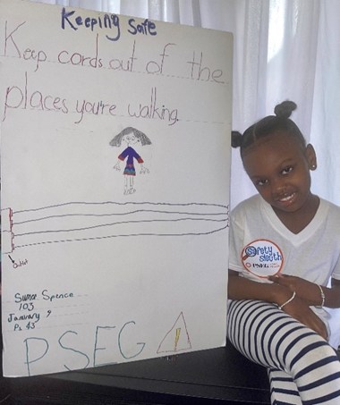 PS 43 first-grader Summer Spence poses with her 'safety sleuth' badge and the electrical safety poster she created that will be featured in PSEG Long Island's Safety Sleuth gallery.